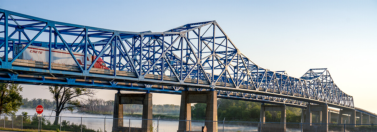 A Crete Carrier truck and dry van cross the Mormon Bridge east of Omaha, Nebraska at dawn.